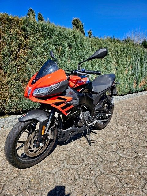 Auf einem gepflasterten Gehweg ist ein rot-schwarzes Motorrad geparkt.