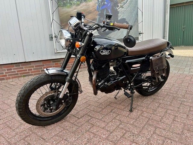 Ein schwarzes Motorrad parkt auf einer gepflasterten Auffahrt neben einem Haus mit grünem Garagentor.