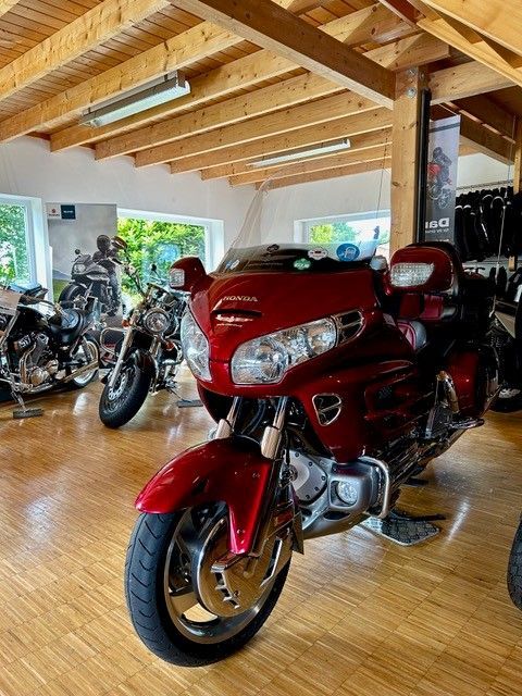 Rotes Honda Gold Wing-Motorrad in einem Ausstellungsraum, mit anderen Motorrädern im Hintergrund, Holzdecke und heller Beleuchtung.