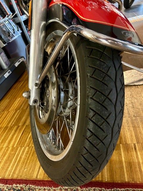 Nahaufnahme eines Motorradvorderrads mit rotem Schutzblech und verchromter Gabel auf einem Holzboden