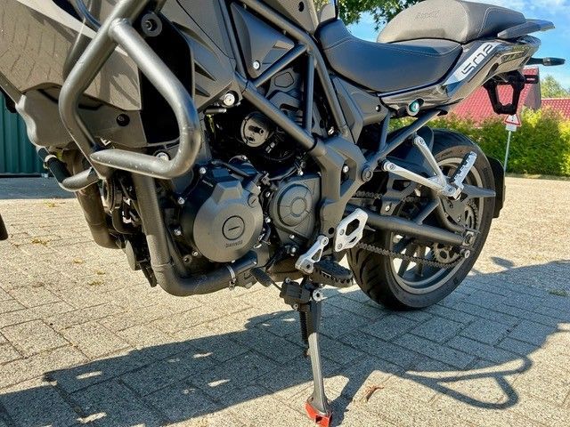 Schwarzes Adventure-Motorrad, geparkt auf einem Seitenständer auf einer sonnenbeschienenen, gepflasterten Auffahrt.
