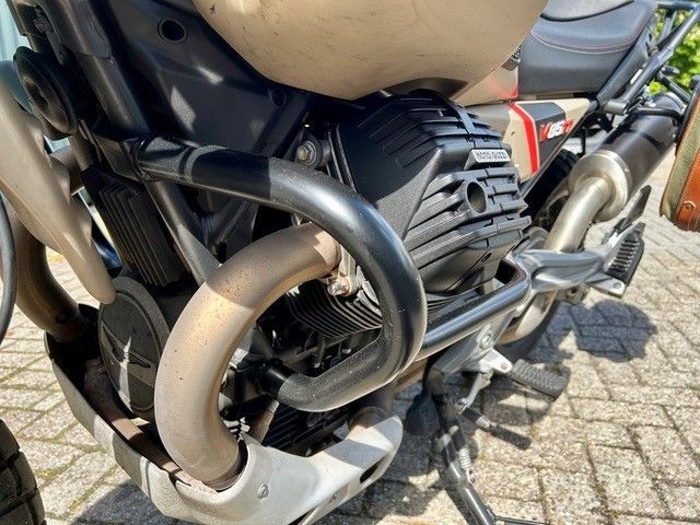 Nahaufnahme eines Motorradmotors und Auspuffrohren auf einer sonnenbeschienenen, gepflasterten Straße