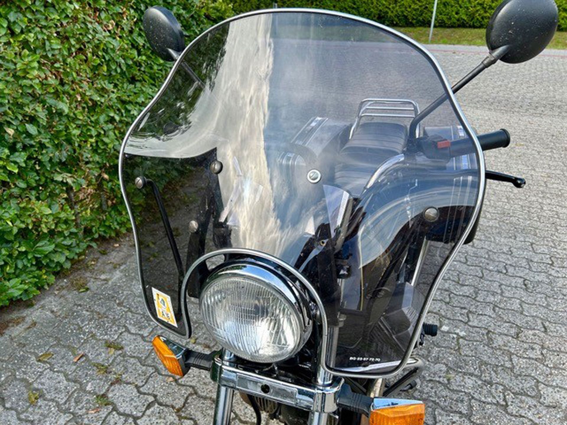 Motorrad mit klarer, dunkler Windschutzscheibe. Nahaufnahme von vorne, Scheinwerfer und orangefarbene Blinker sichtbar, im Freien geparkt.