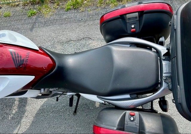 Ein rot-weißes Honda-Motorrad mit schwarzem Sitz und Satteltaschen auf dem Bürgersteig.