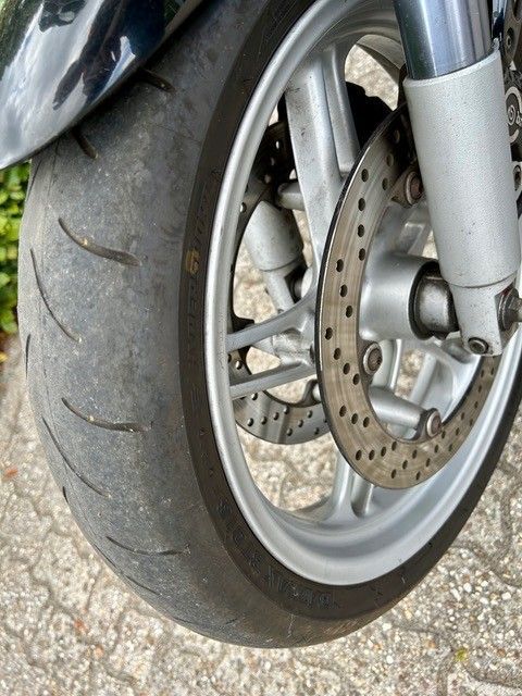 Motorrad-Vorderreifen, abgefahrenes Profil sichtbar, mit silbernem Rad und Bremsscheibe.