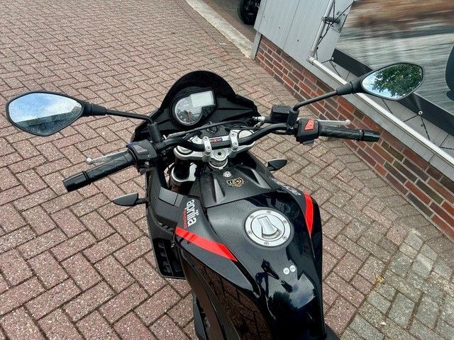 Ein schwarzes Sportmotorrad parkt auf einer gepflasterten Auffahrt neben einem Gebäude.