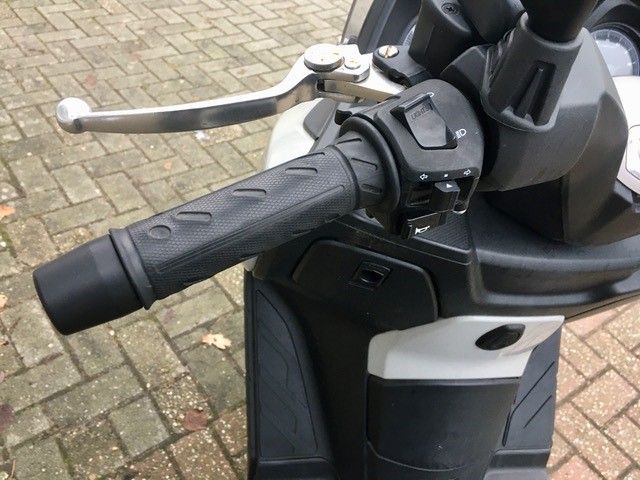 Eine Nahaufnahme des Lenkers eines Rollers auf einem gemauerten Bürgersteig