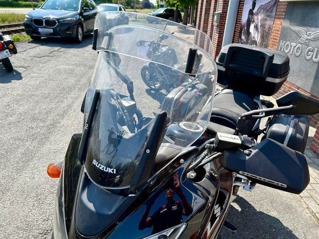 Vor einem Gebäude parkt ein schwarzes Suzuki-Motorrad.