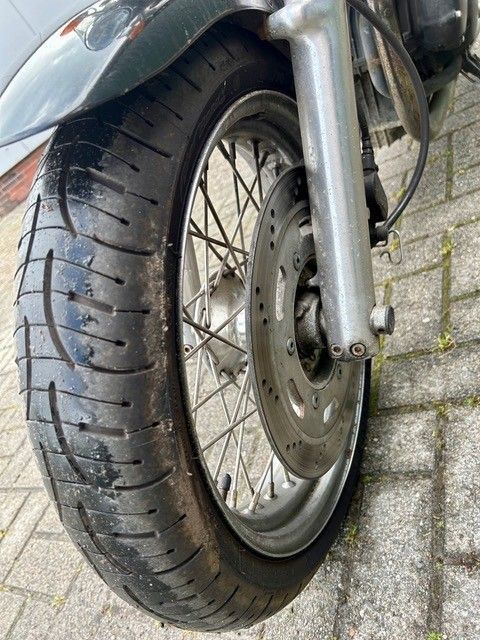 Nahaufnahme eines Motorradvorderrads mit Reifen auf einer asphaltierten Straße.