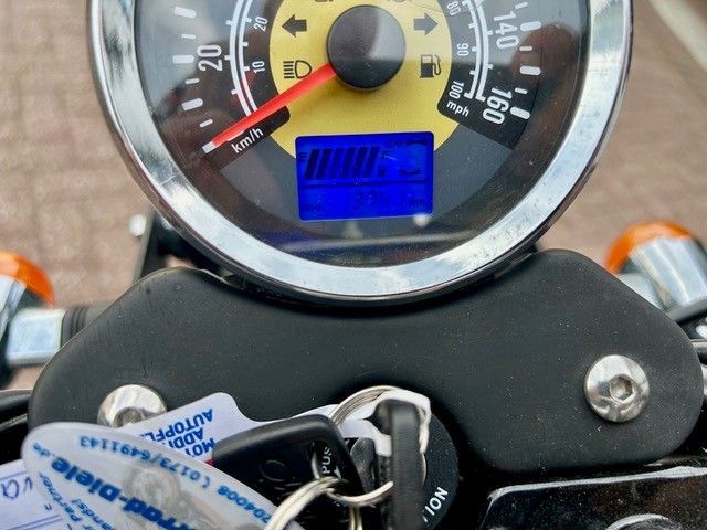 Nahaufnahme eines Motorradtachos und Zündschlüssels mit blauer Digitalanzeige und rotem Zeiger.