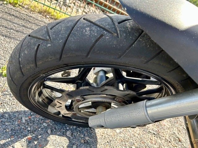 Motorrad-Hinterrad mit schwarzem Reifen, schwarzer Felge, silbernem Auspuff und Bremsscheibe.