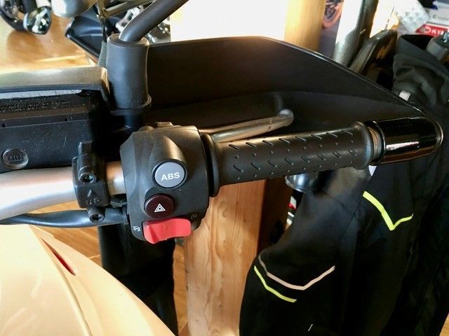 Eine Nahaufnahme eines Motorradlenkers mit einem roten Knopf mit der Aufschrift „ABS“