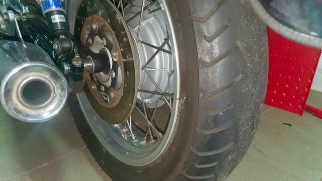 Motorradhinterrad mit Reifen, Bremsscheibe und Auspuffrohr. Silber und schwarz.