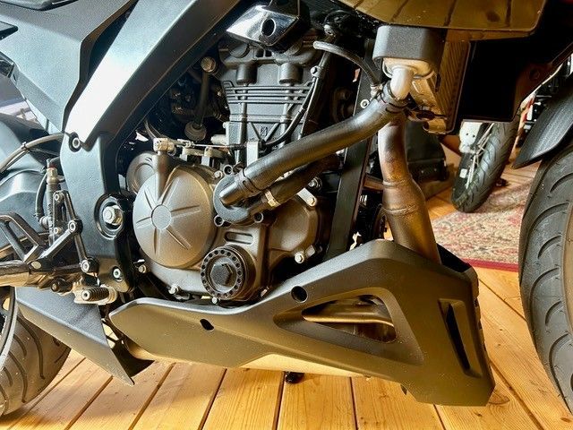 Nahaufnahme eines Motorradmotors und -auspuffs, goldene Verkleidung und Hinterrad sind sichtbar.
