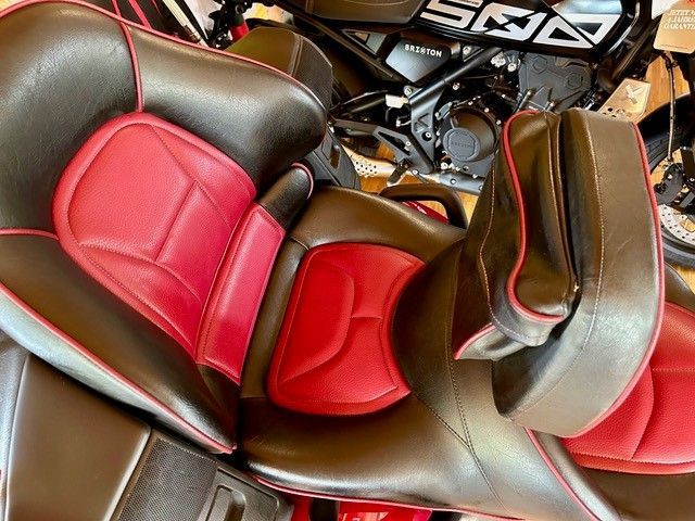 Nahaufnahme eines Motorradsitzes mit roter und schwarzer Lederpolsterung, einer Rückenlehne und roter Paspelierung.