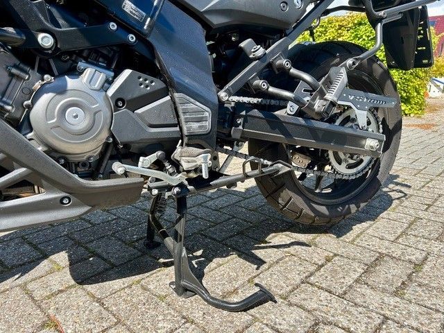 Nahaufnahme eines Motorrads mit heruntergeklapptem Hauptständer auf einem gepflasterten Untergrund.
