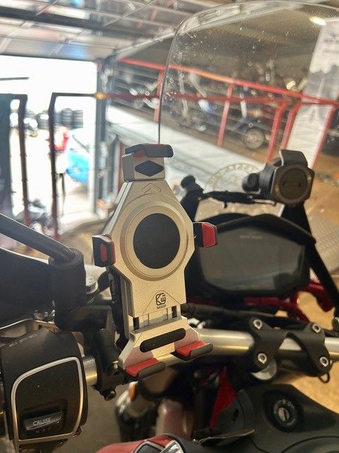 Motorradlenker mit beiger Handyhalterung in einer Garage, im Hintergrund weitere Motorräder.