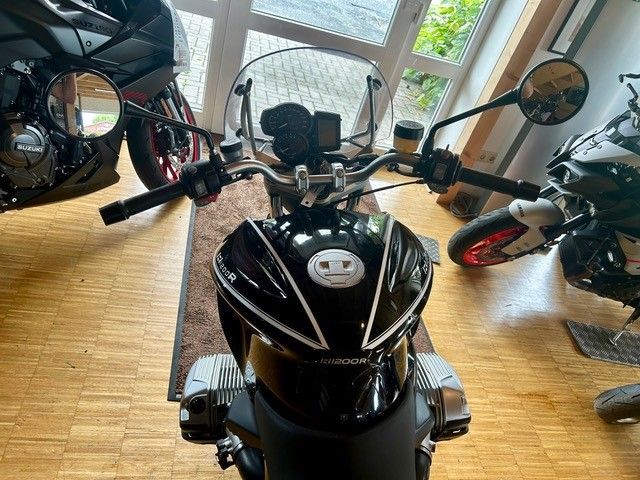 Ein schwarzer Roller steht drinnen auf einem Holzboden, flankiert von anderen Motorrädern in der Nähe eines Fensters.