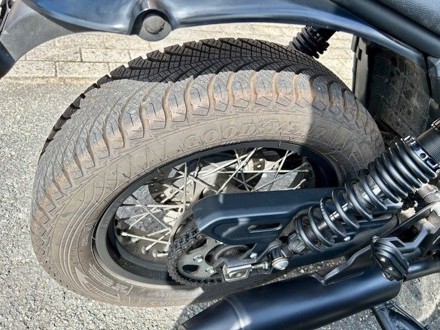 Motorrad-Hinterreifen mit abgefahrenem Profil, schwarzer Felge und Aufhängungskomponenten.