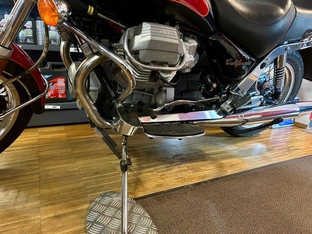 Schwarzes Motorrad auf dem Seitenständer, verchromter Motor und Auspuff auf einem Holzboden im Ausstellungsraum.