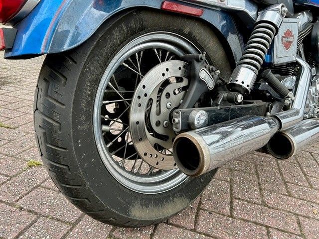 Rückansicht eines blauen Harley-Davidson-Motorrads mit Hinterreifen, Auspuffrohren und Aufhängung. Das Motorrad steht auf einer Ziegelfläche.