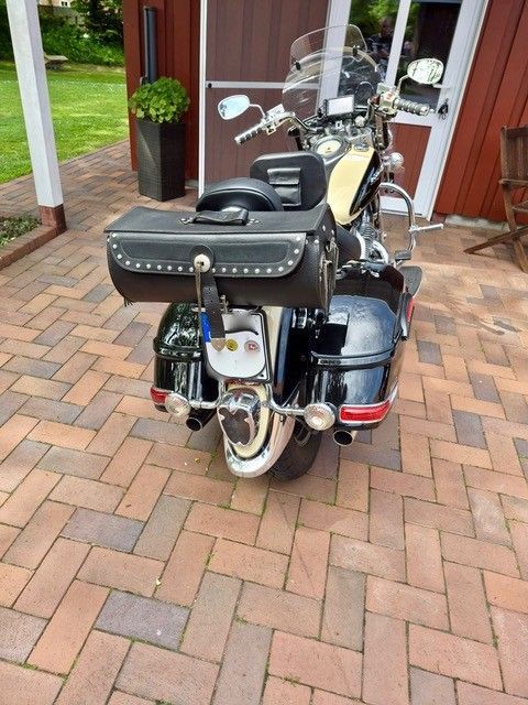 Schwarzes Motorrad mit Satteltaschen parkt auf einer gepflasterten Auffahrt vor einem Haus.