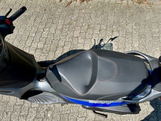 Ein schwarz - blauer Motorroller ist auf einem gepflasterten Gehweg geparkt.