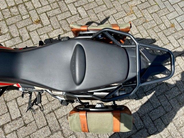 Draufsicht auf ein geparktes Motorrad mit schwarzem Sitz und orangefarbener Tasche auf Backsteinpflaster