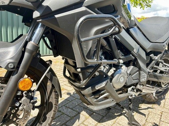 Graues Adventure-Motorrad, geparkt auf einer asphaltierten Fläche; Nahaufnahme von Motor, Sturzbügeln und Vorderrad.