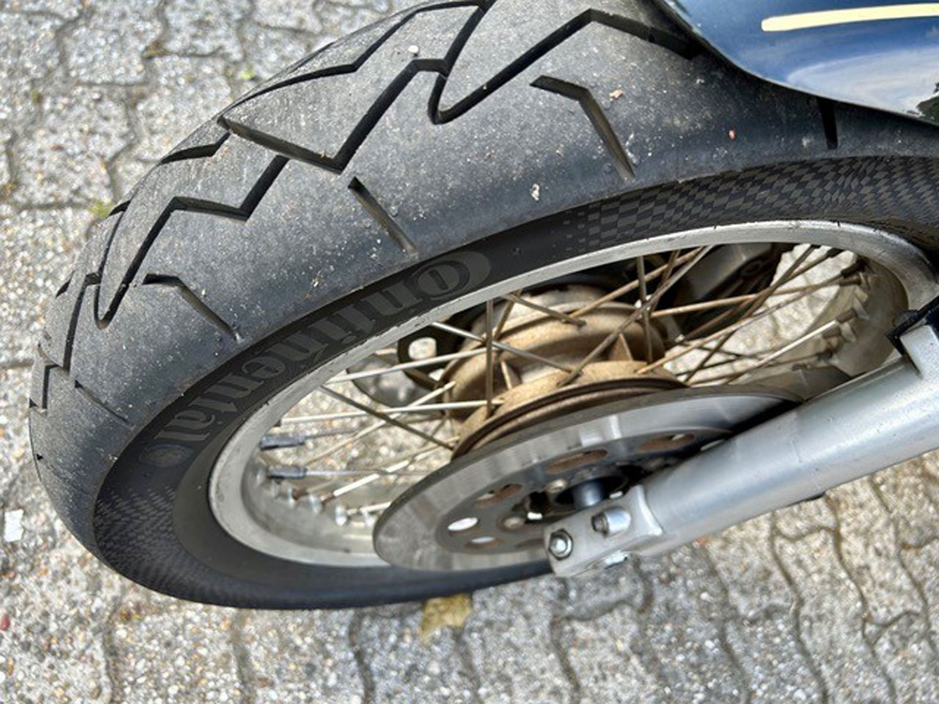 Motorrad-Hinterrad mit Continental-Reifen. Silberne Felge, Bremsscheibe und Auspuffrohr sichtbar.