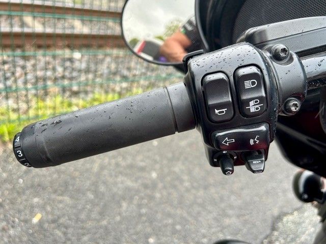 Motorradlenker mit Bedienelementen, Spiegel und schwarzem Griff vor dem Hintergrund einer Straße