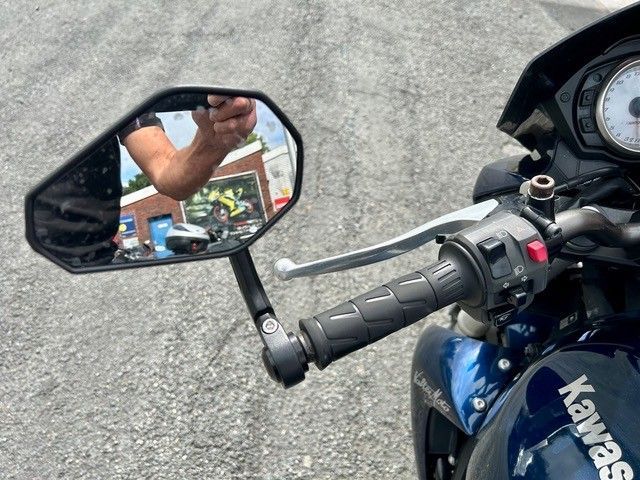 Motorradlenker und Spiegel auf dem Bürgersteig, im Spiegel spiegelt sich der Arm des Fahrers.