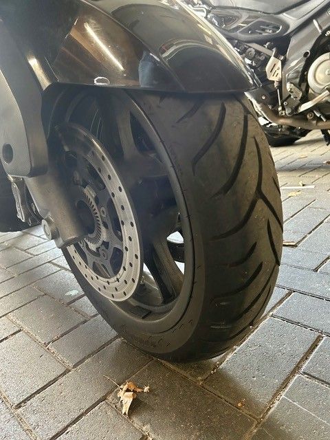 Nahaufnahme eines schwarzen Motorradvorderrads und einer Bremsscheibe auf einem gepflasterten Boden.