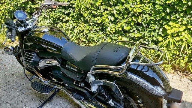 Schwarzes Motorrad mit Chrom-Akzenten, geparkt auf einer gemauerten Terrasse, mit grünem Laub im Hintergrund.