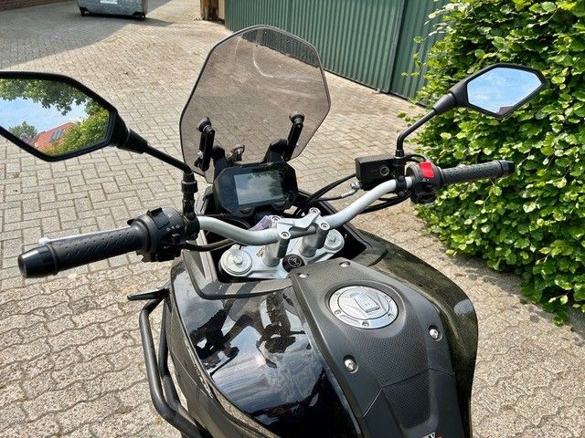 Ein schwarzes Motorrad ist auf einer Ziegelsteinstraße neben einem Busch geparkt.
