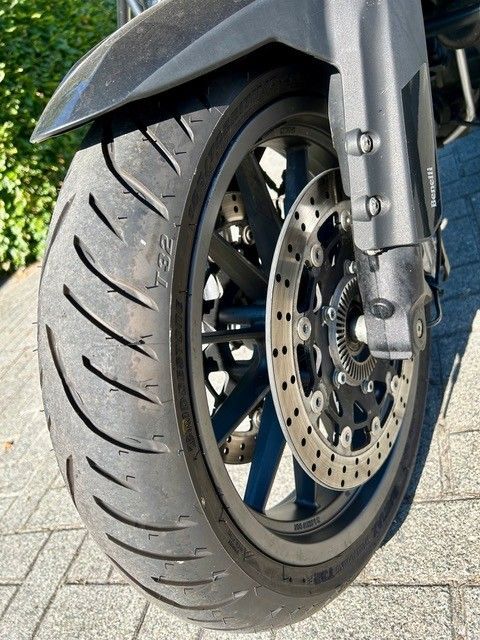 Nahaufnahme eines Motorradvorderrads mit Scheibenbremse und schwarzem Reifen auf Asphalt