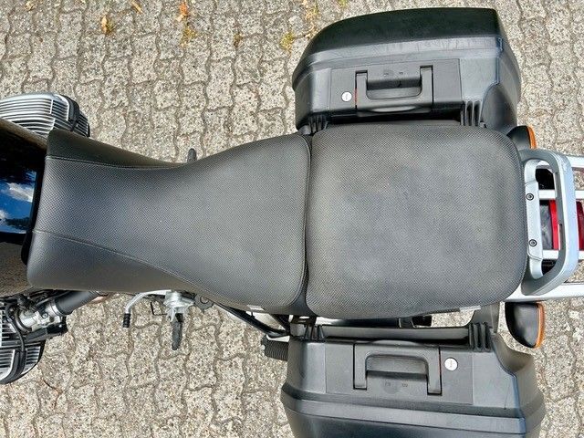 Draufsicht auf einen schwarzen Motorradsitz mit Aufbewahrungskoffern auf gepflastertem Boden.