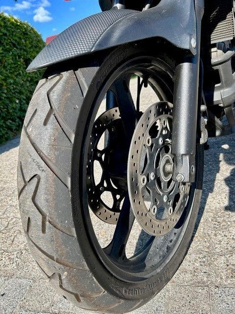 Nahaufnahme eines Motorradvorderrads und einer Bremsscheibe auf einer sonnigen Straße