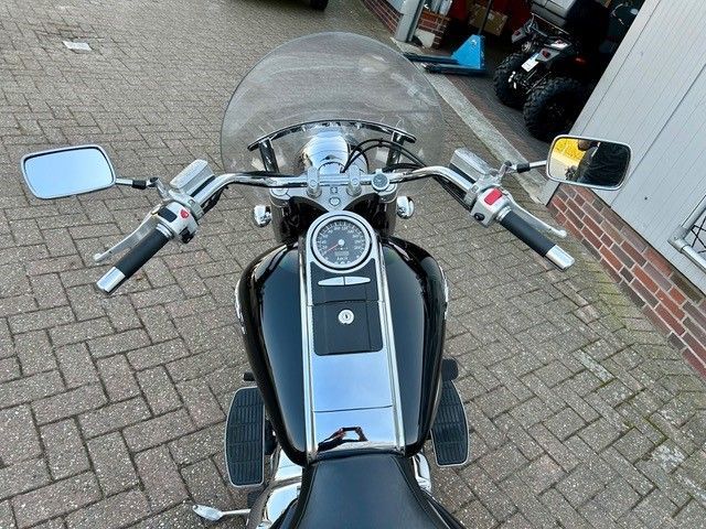 Auf einem gepflasterten Gehweg ist ein schwarzes Motorrad mit Windschutzscheibe geparkt.