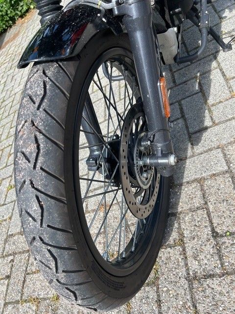 Nahaufnahme eines Motorradvorderrads mit Scheibenbremse auf einer asphaltierten Fahrbahn.