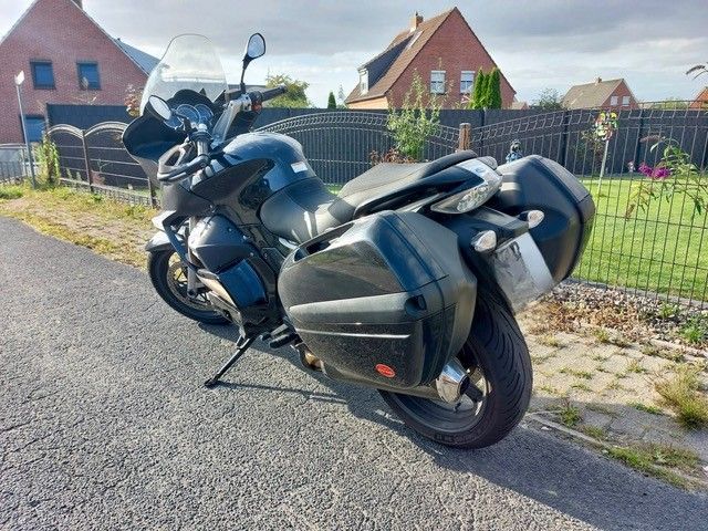 Schwarzes Tourenmotorrad mit Hartschalen-Seitenkoffern auf einer Asphaltstraße vor einem Wohnhaus geparkt.