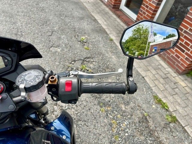Rechter Lenker und Spiegel eines Motorrads, geparkt neben einer Backsteinmauer auf einem gepflasterten Gehweg.