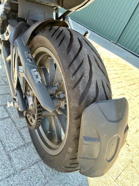 Nahaufnahme des Hinterrads eines Motorrads mit profiliertem schwarzem Reifen und grauem Schutzblech im Sonnenlicht