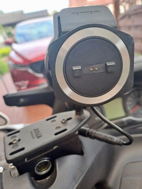 Eine Motorrad-GPS-Halterung mit einem TomTom-Gerät und einem Ladekabel. Die Halterung ist schwarz und silber und wird am Lenker befestigt.