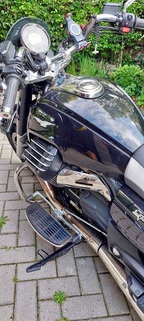 Schwarzes Motorrad auf einer Ziegelfläche geparkt, Chrom-Akzente, vor grünem Laub.