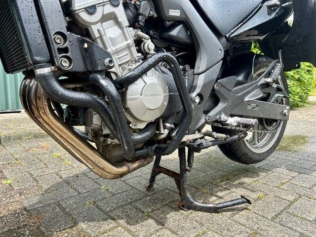 Nahaufnahme eines Motorrads mit beschädigtem Auspuffrohr, das auf einer gepflasterten Einfahrt liegt.
