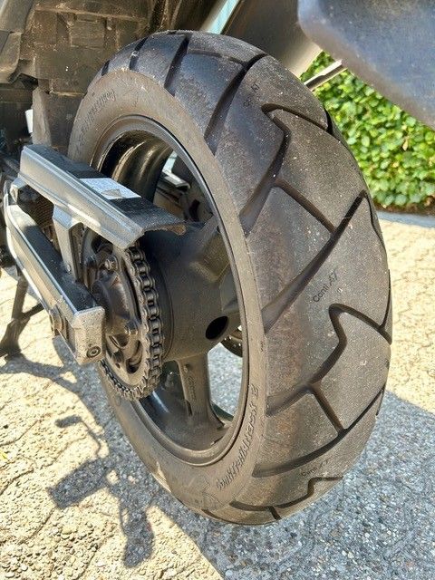 Nahaufnahme eines Motorradhinterrads und -reifens auf sonnenbeschienenem Asphalt.