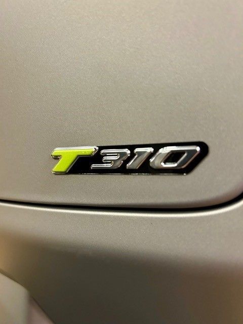 Silbernes Autoemblem: „T 310“ mit neongrünem „T“ auf einem silbernen Auto.