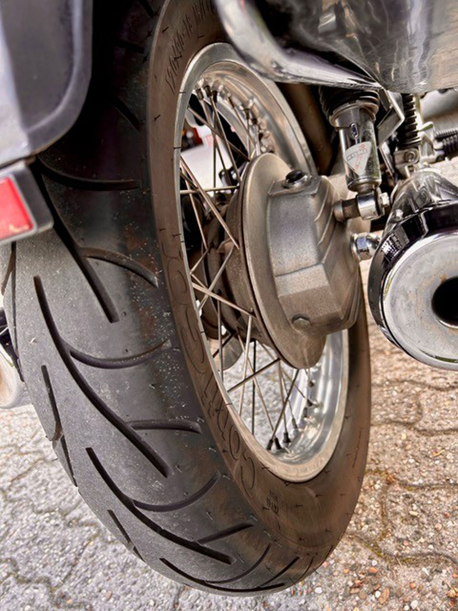 Nahaufnahme des Hinterreifens und Rads eines Motorrads. Der schwarze Reifen hat Profil, ein Chromrad mit Speichen und eine silberne Bremstrommel.