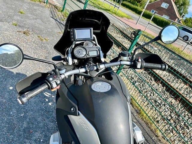 Schwarze Motorradlenkeransicht mit Spiegeln, GPS und Handschützern. Draußen, sonnig.